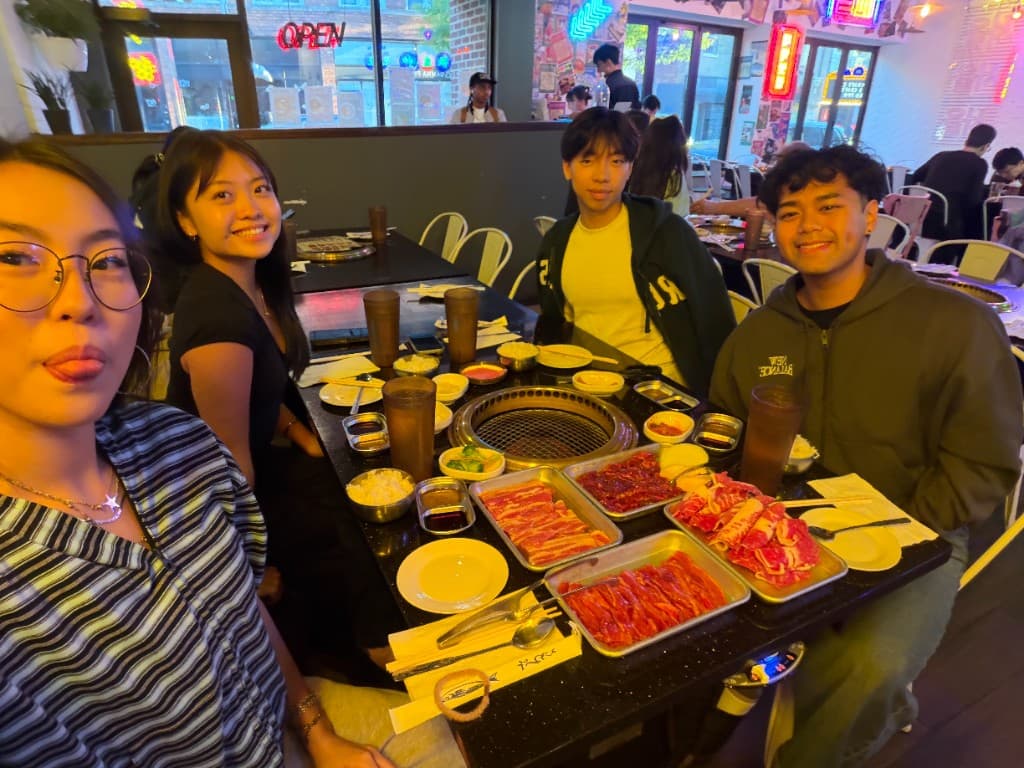 Four friends around a Korean BBQ table, smiling at the camera.