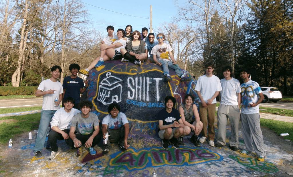 SHIFT Creator Space members outdoors around a painted banner bearing the group's logo.